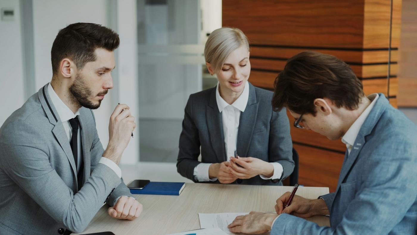 Advogada conversando com dois clientes numa mesa de reunião