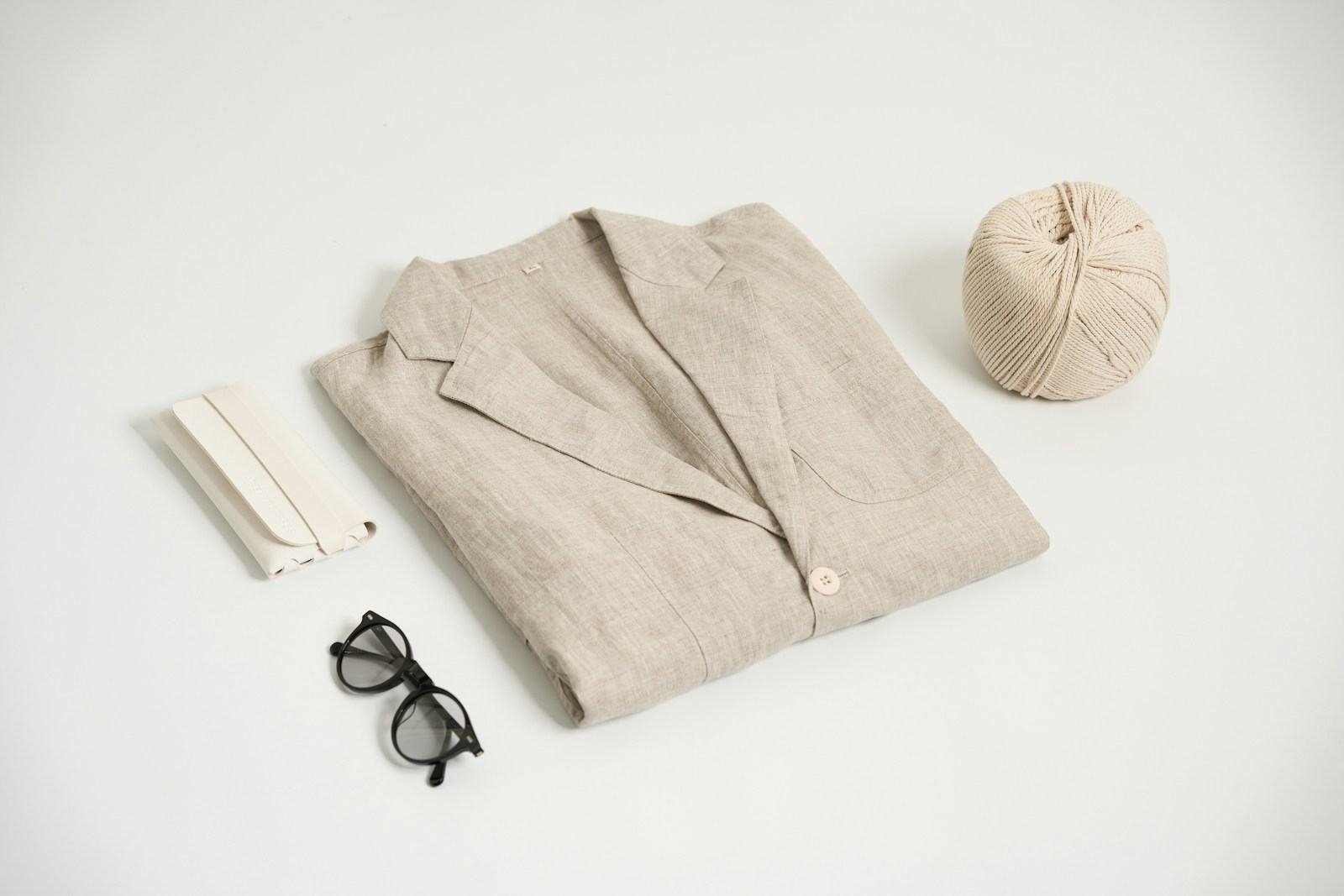 Blazer de linho dobrado ao lado de um novelo, óculos e fita de tecido