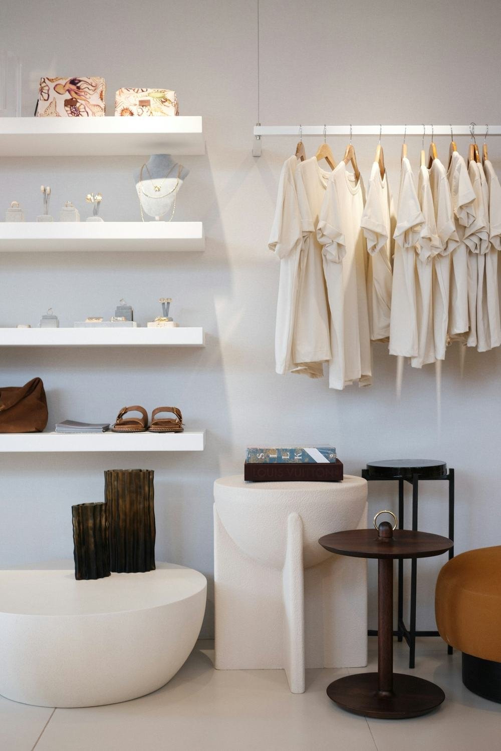 Interior do ateliê, com araras de roupas claras e prateleiras